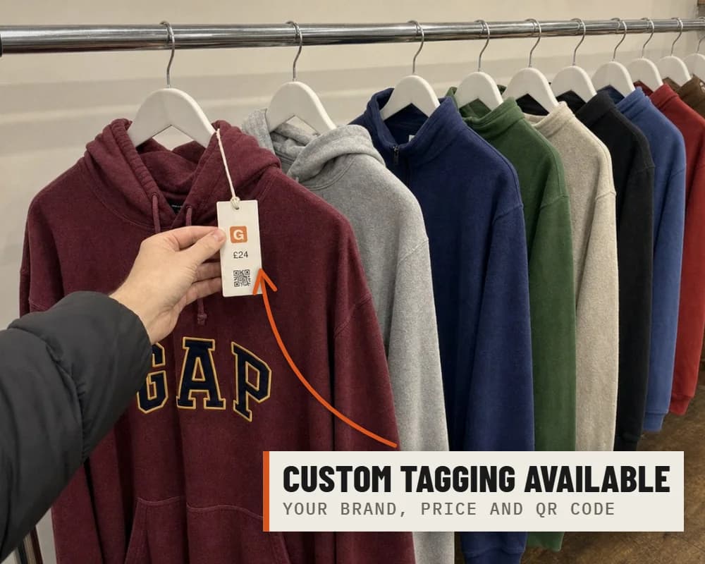 A hand holding up the branded swing tag, with a price and QR code, on a Gap hoodie on a shop rail