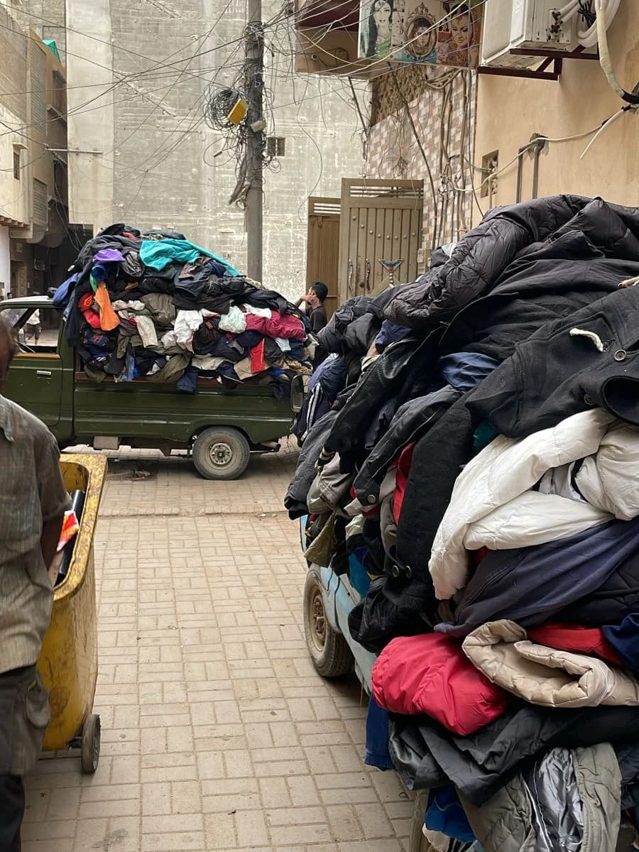 A Pakistan street, pickups piled high with second-hand clothes